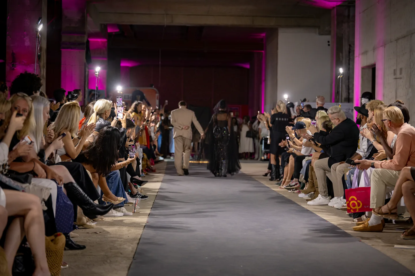 Wide runway scene with guests capturing the finale.
